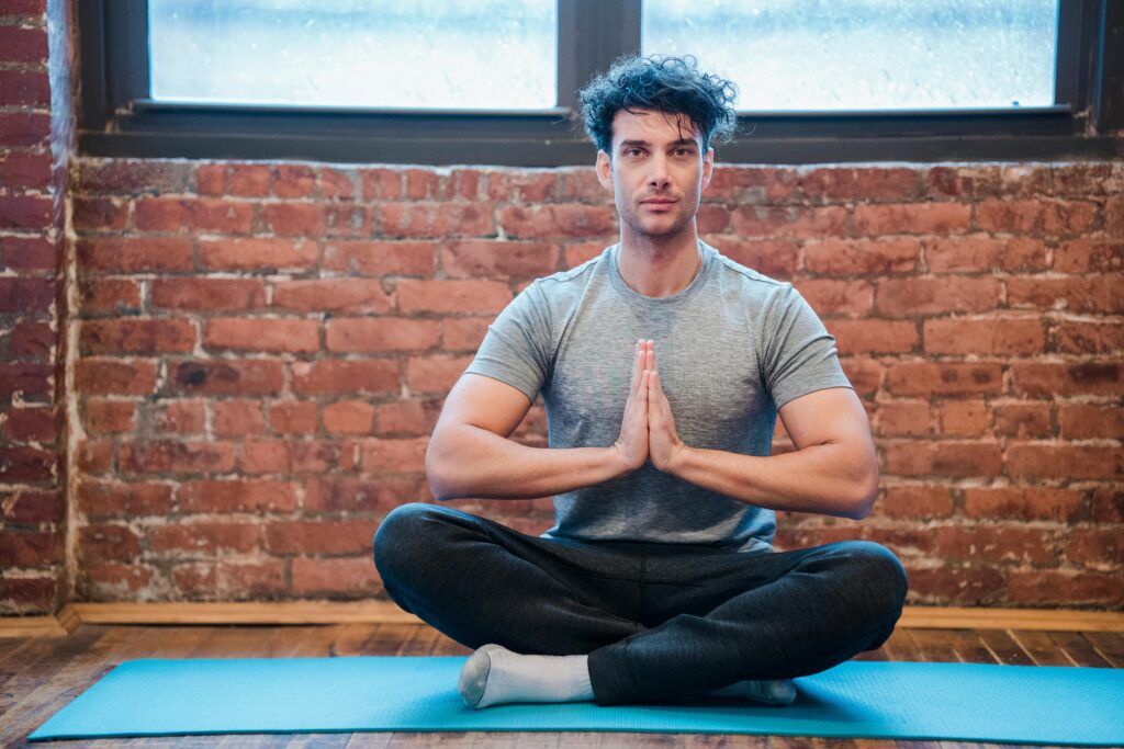 Full body of focused male sitting in Sukhasana with praying hands while practicing yoga on sports mat