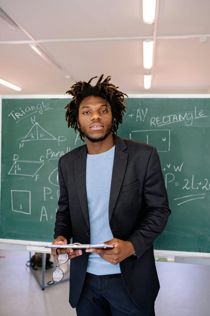 Confident teacher stands in a classroom, illustrating geometric concepts on a chalkboard.